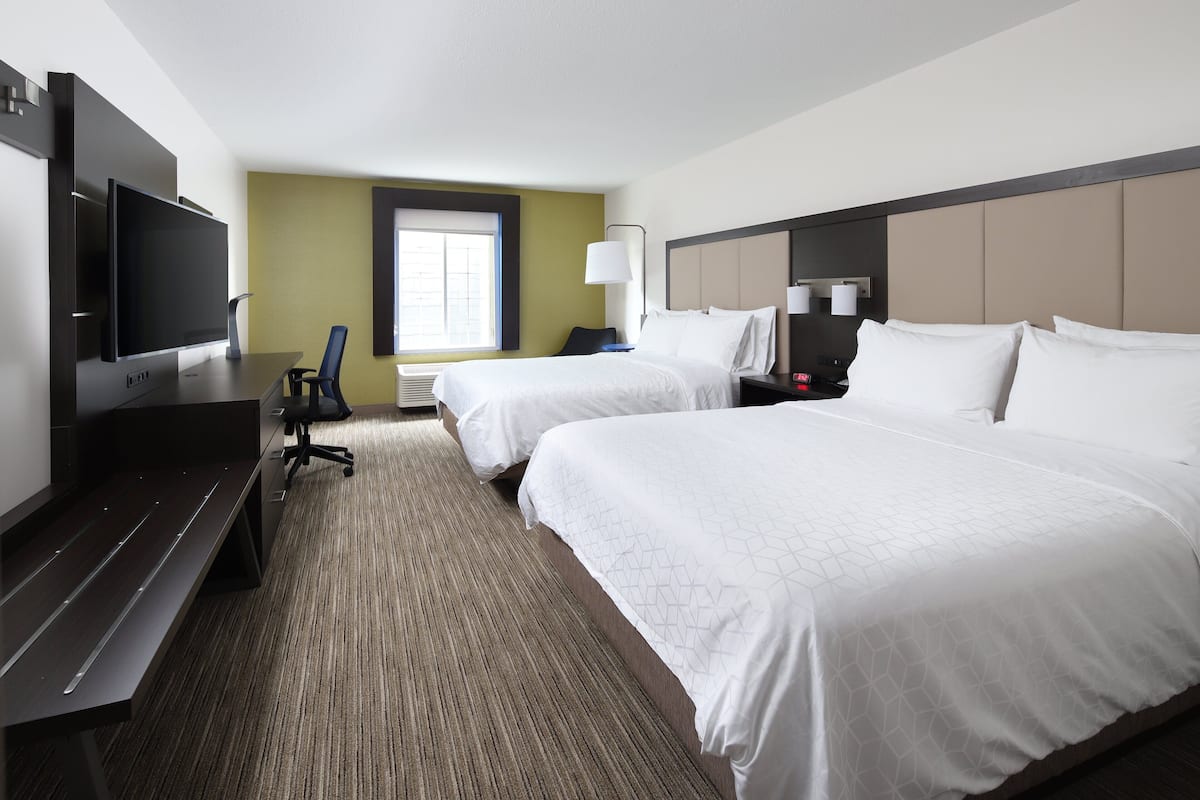A hotel room with two beds, a desk with a flat-screen TV, a chair, and a window with blinds.