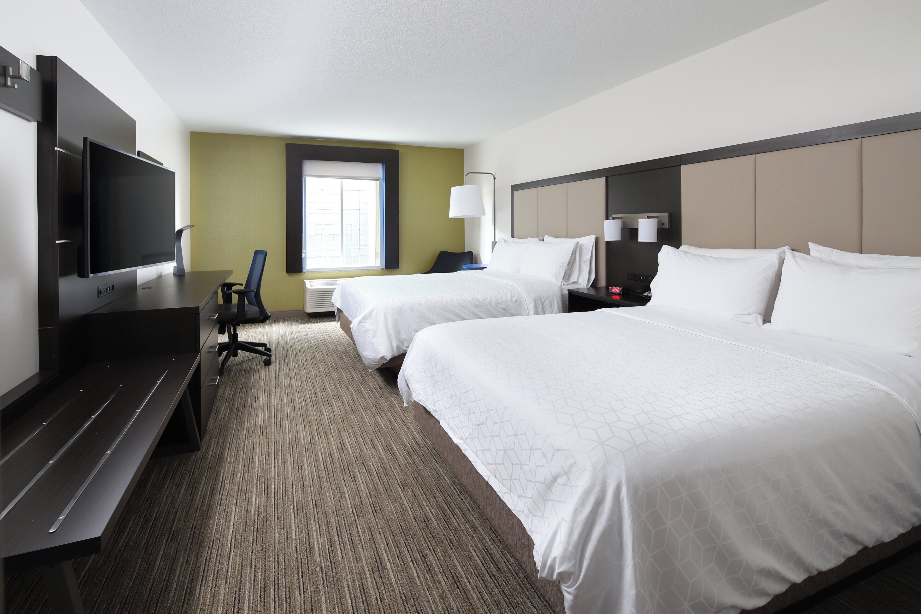 A hotel room with two beds, a TV, a desk, and a chair.