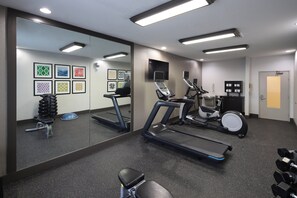 Ein Fitnessraum mit Trainingsgeräten, einem Spiegel und Kunstwerken an den Wänden.