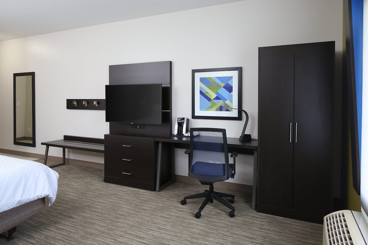 A hotel room with a bed, a desk with a computer, a chair, a wardrobe, and a television.