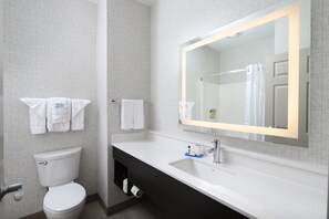A modern bathroom with a white toilet, a large mirror, and a black vanity. - Holiday Inn Express Grand Rapids SW by IHG (Grandville)