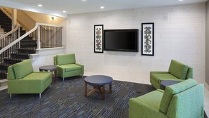 A lobby with a staircase, green upholstered seating, a flat-screen TV, and patterned carpet. - Holiday Inn Express Grand Rapids SW by IHG (Grandville)
