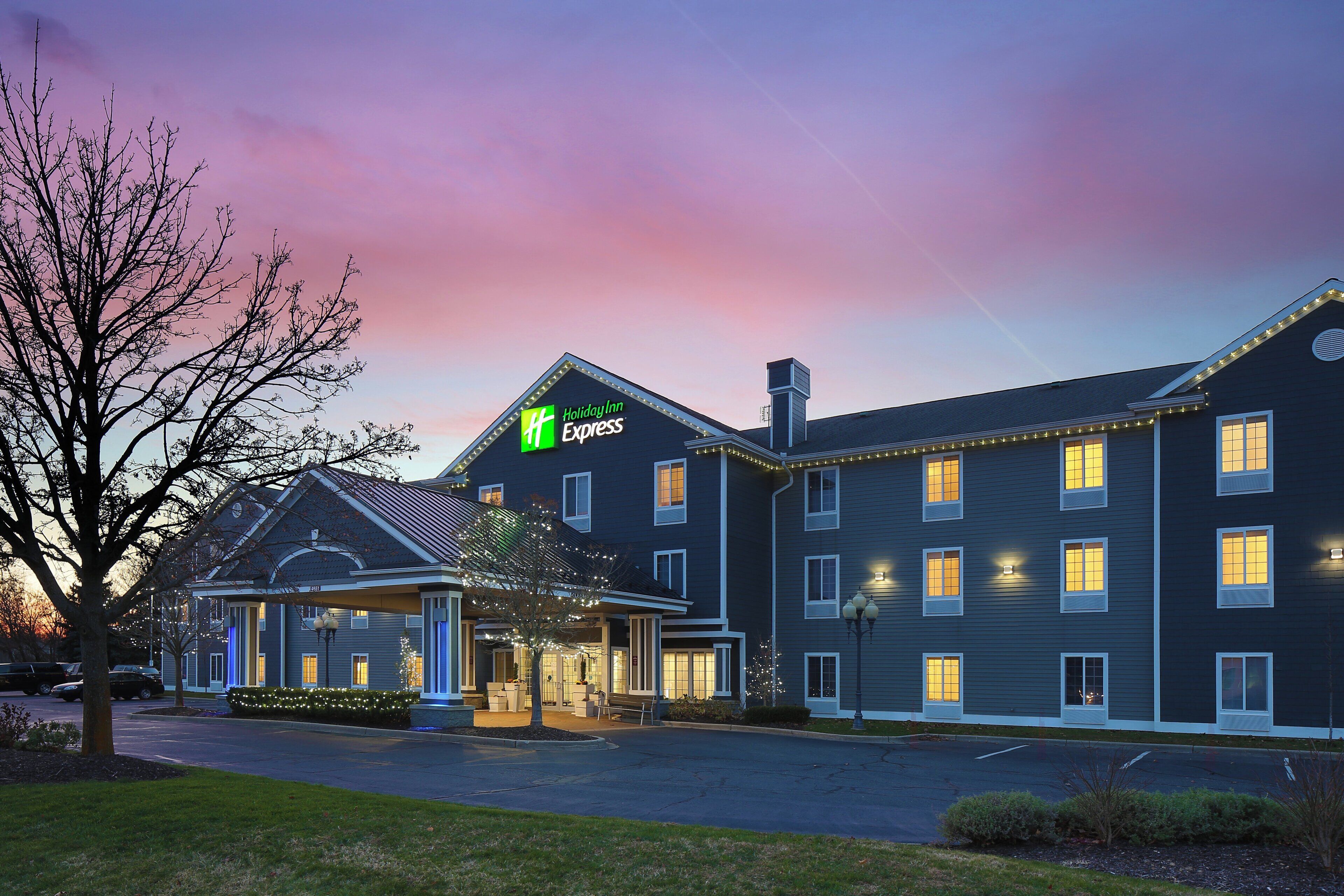 Un hotel Holiday Inn Express con vestíbulo techado, varias ventanas y una entrada con jardines.