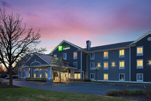 Un hotel Holiday Inn Express con vestíbulo techado, varias ventanas y una entrada con jardines.