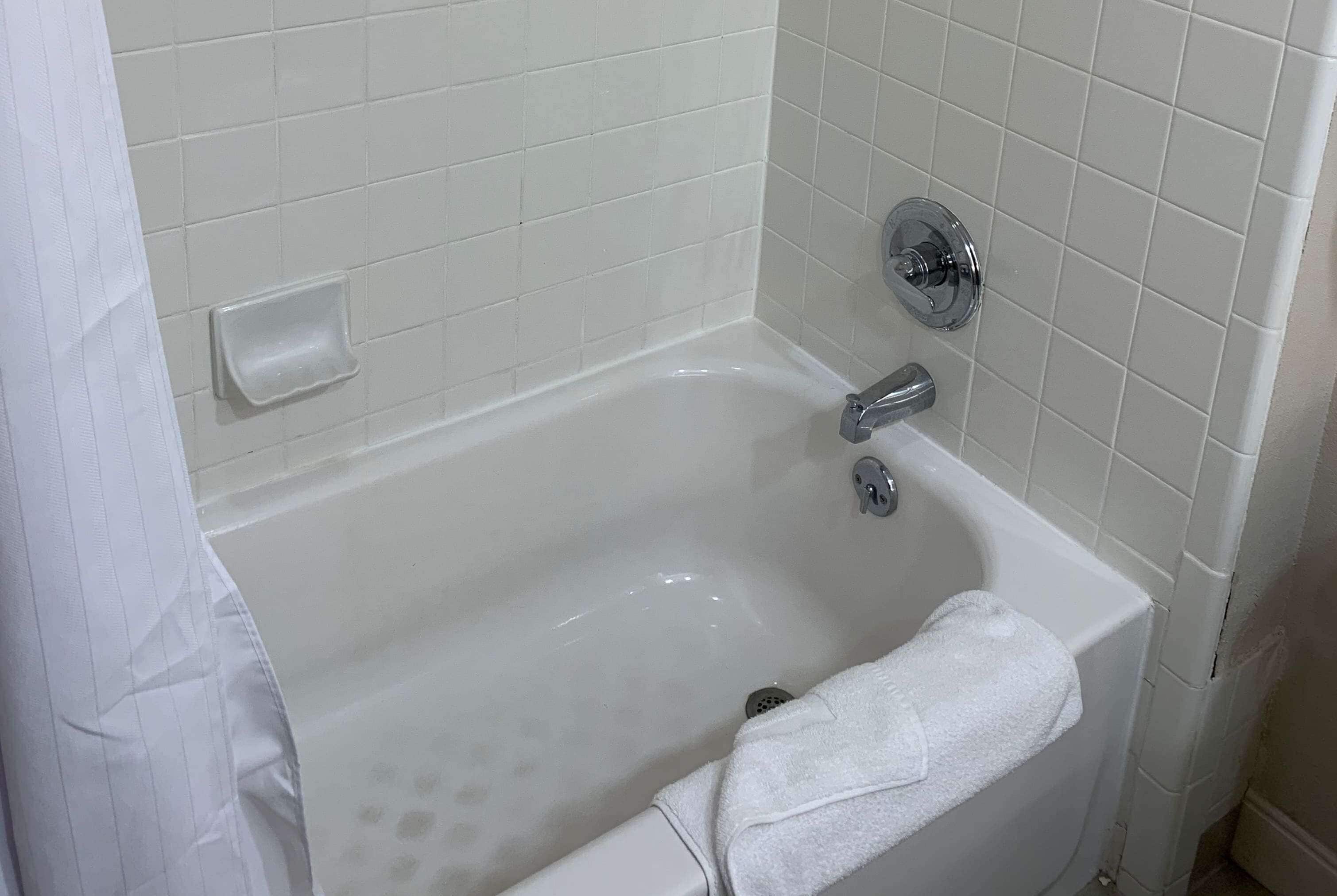 Une baignoire blanche avec un robinet chromé, une serviette blanche et un porte-savon fixé au mur.