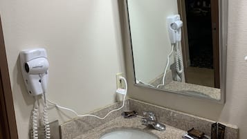 Un baño con encimera de granito, un lavabo blanco, un espejo y un secador de pelo montado en la pared.