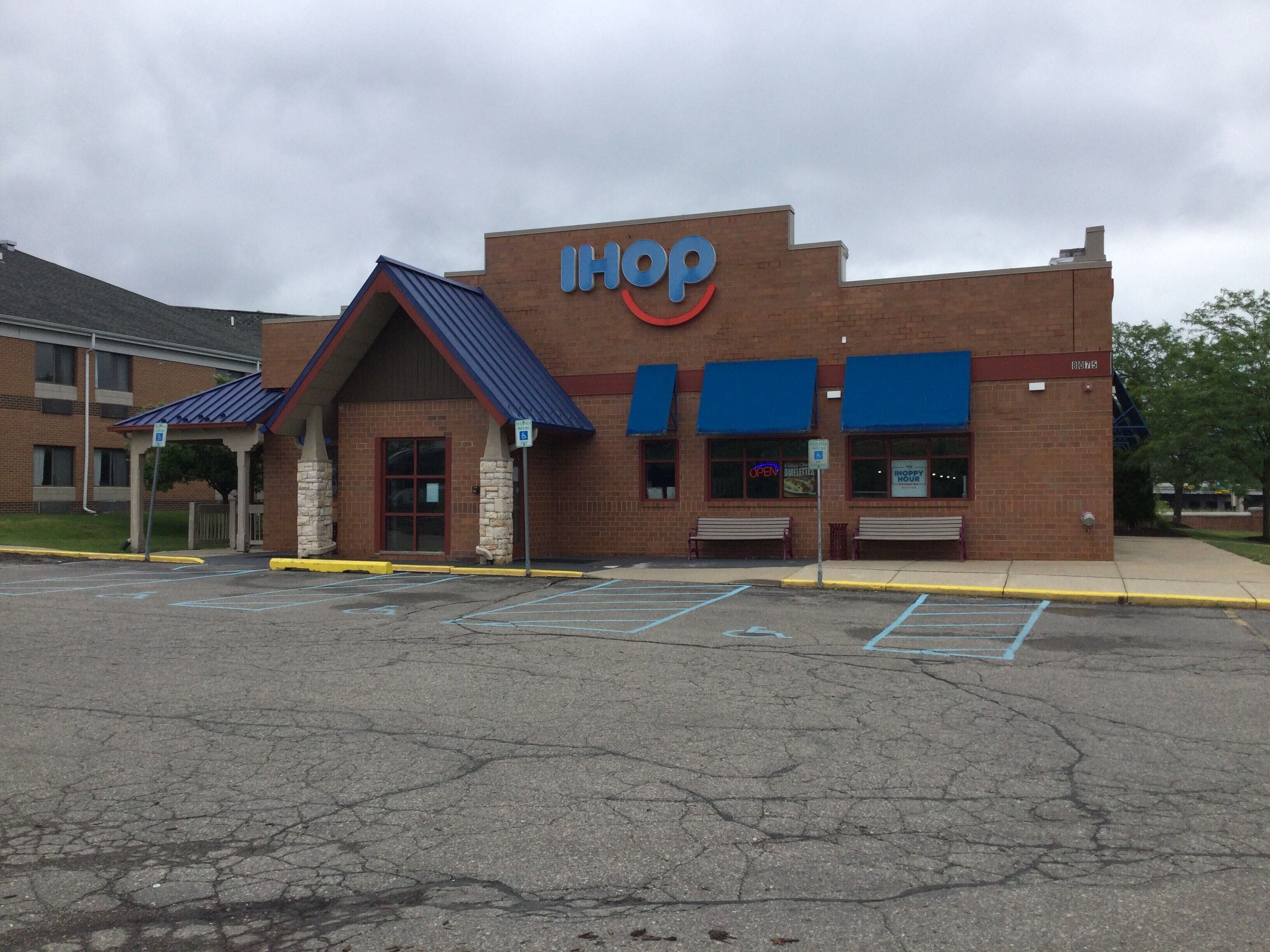 A IHOP restaurant with a brick facade, blue awnings, and a parking lot in front.