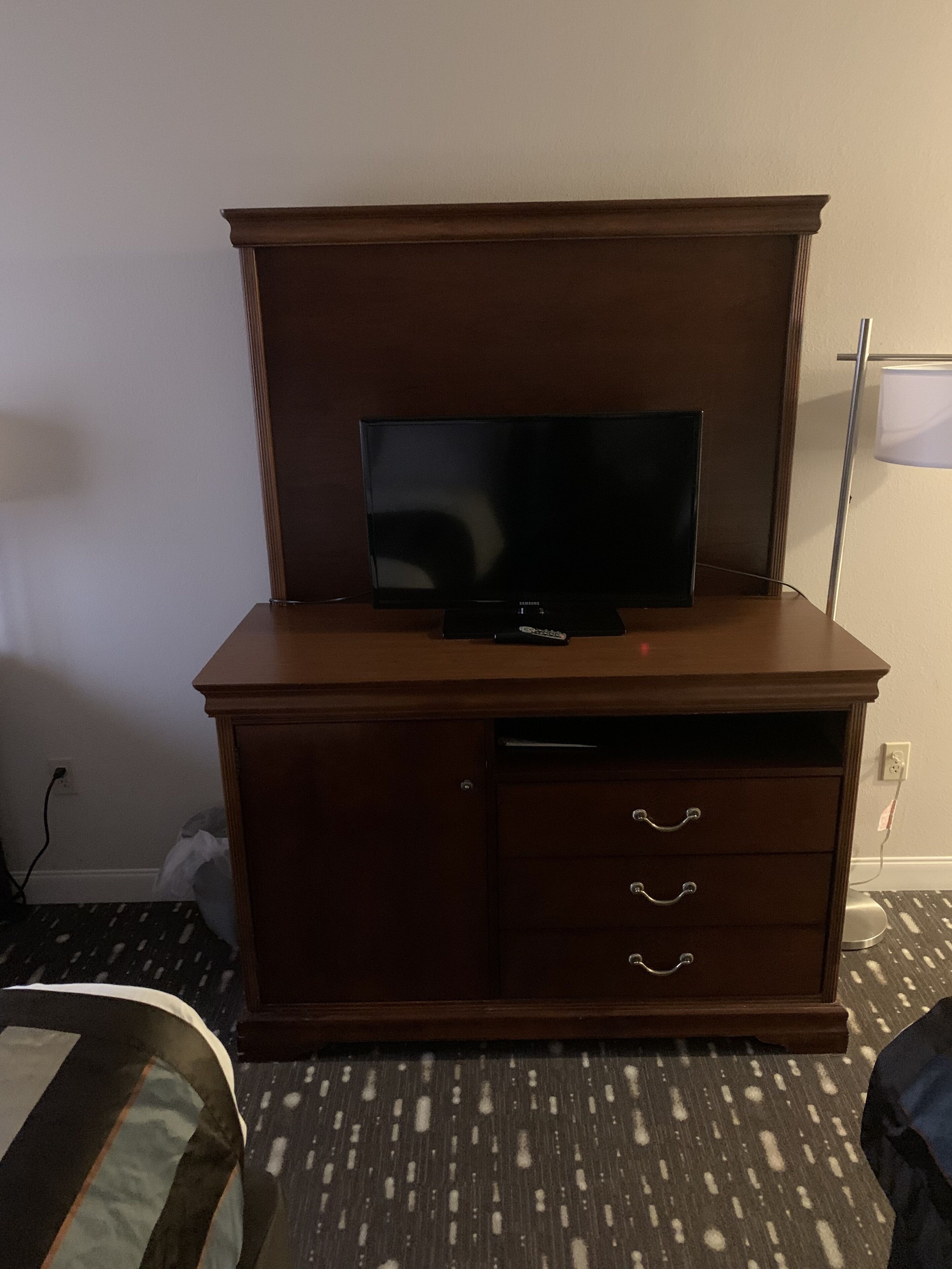 Un mueble de madera con un televisor de pantalla plana encima, un cajón con tiradores metálicos y una lámpara a la derecha.