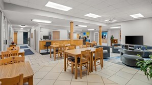 A spacious indoor area with wooden tables and chairs, a reception desk, a television, and a seating area with sofas. - Days Inn by Wyndham Imlay City (Imlay City)