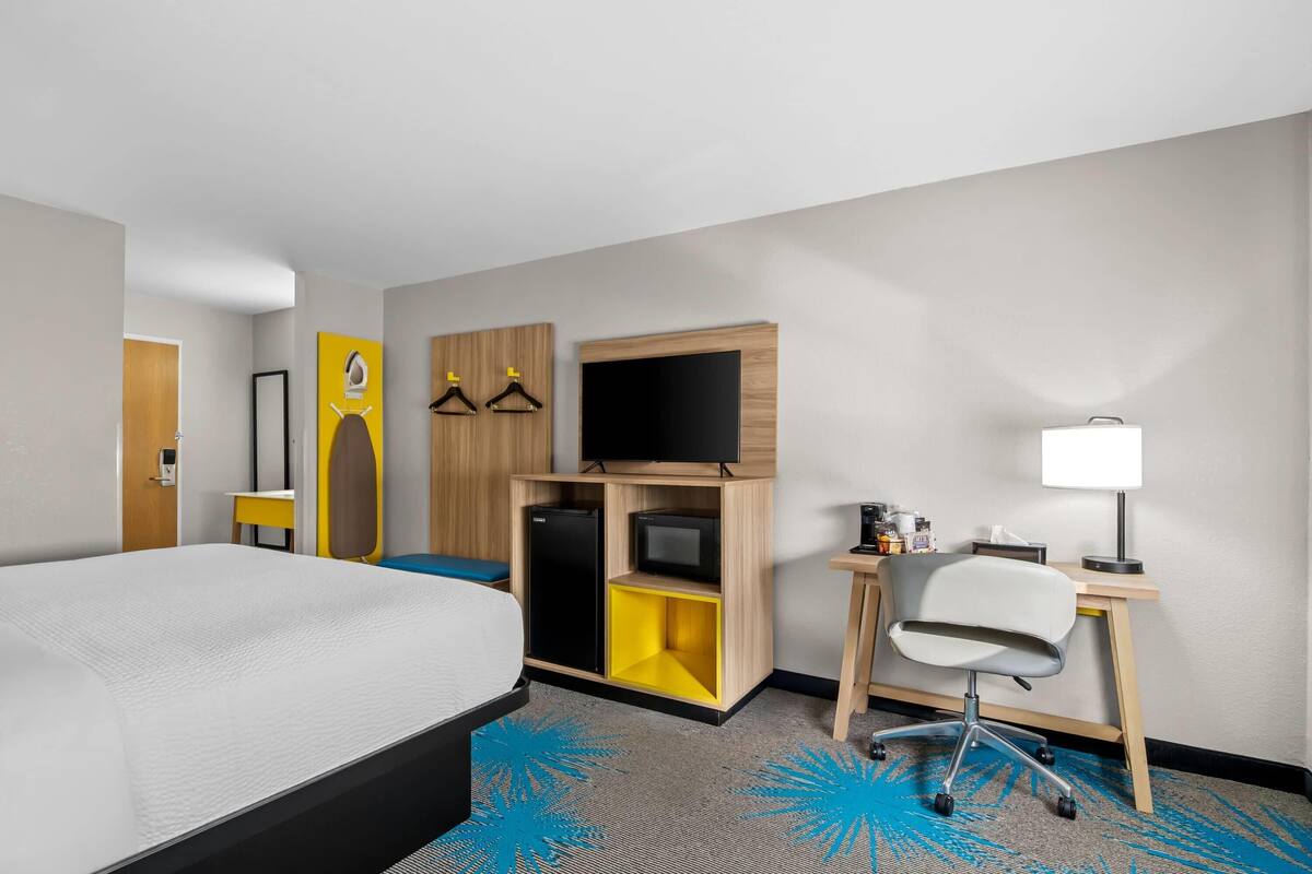 A hotel room with a bed, a desk with a chair, a television, and a small refrigerator.