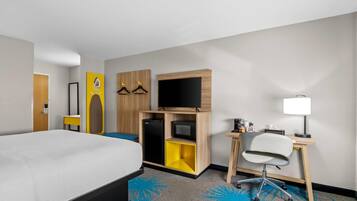A hotel room with a bed, a desk with a chair, a television, and a small refrigerator.