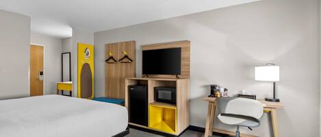 A hotel room with a bed, a desk with a chair, a television, and a small refrigerator.