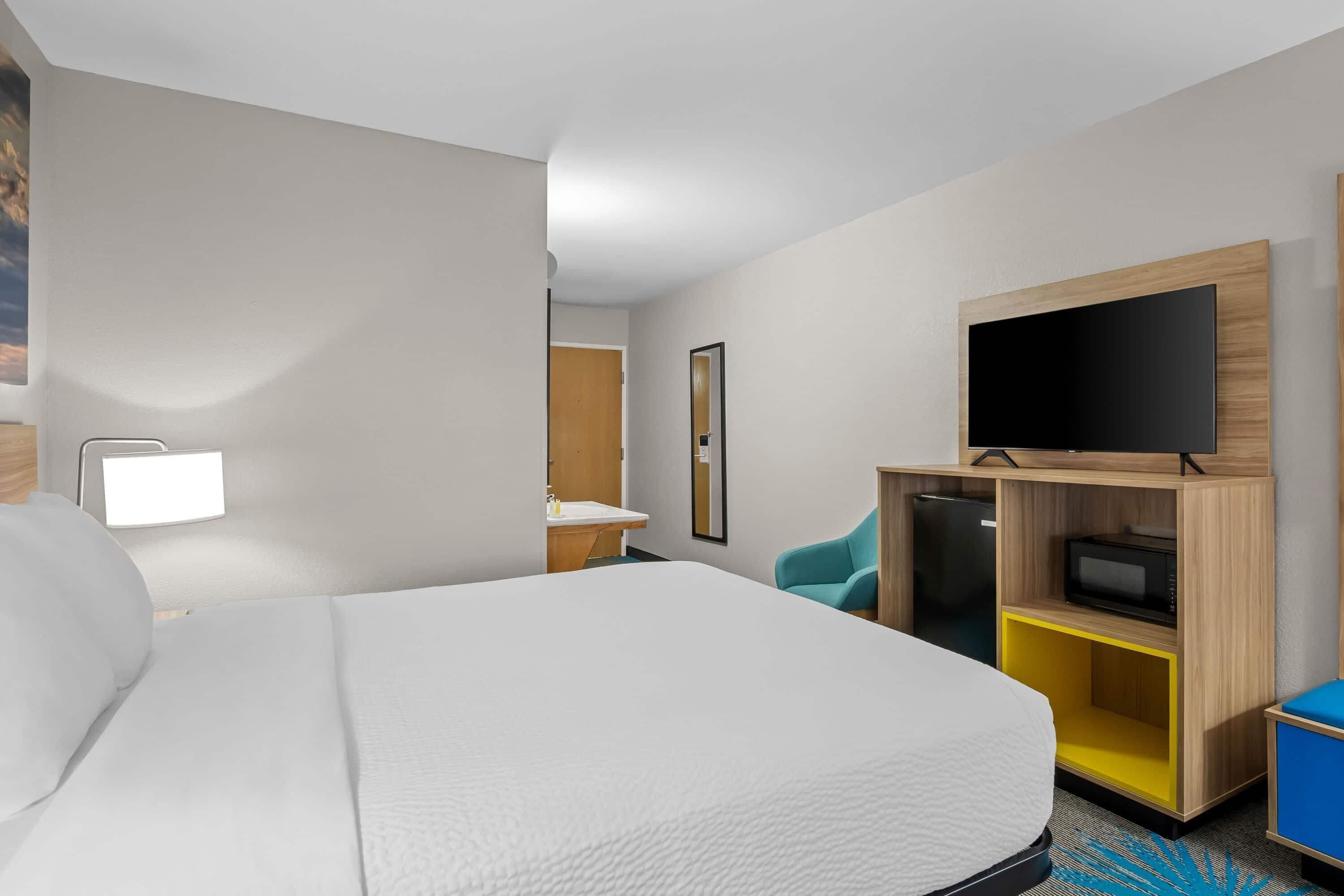 A hotel room with a large bed, a television on a wooden stand, a desk with a chair, and a bathroom visible through an open door.