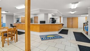 A reception area with a wooden reception desk, a seating area with a table and chairs, and a doormat with the Days Inn logo. - Days Inn by Wyndham Imlay City (Imlay City)