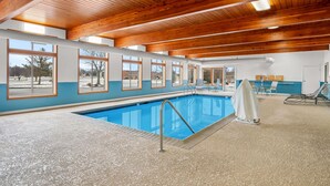An indoor swimming pool with wooden beams, large windows, and lounge chairs. - Days Inn by Wyndham Imlay City (Imlay City)