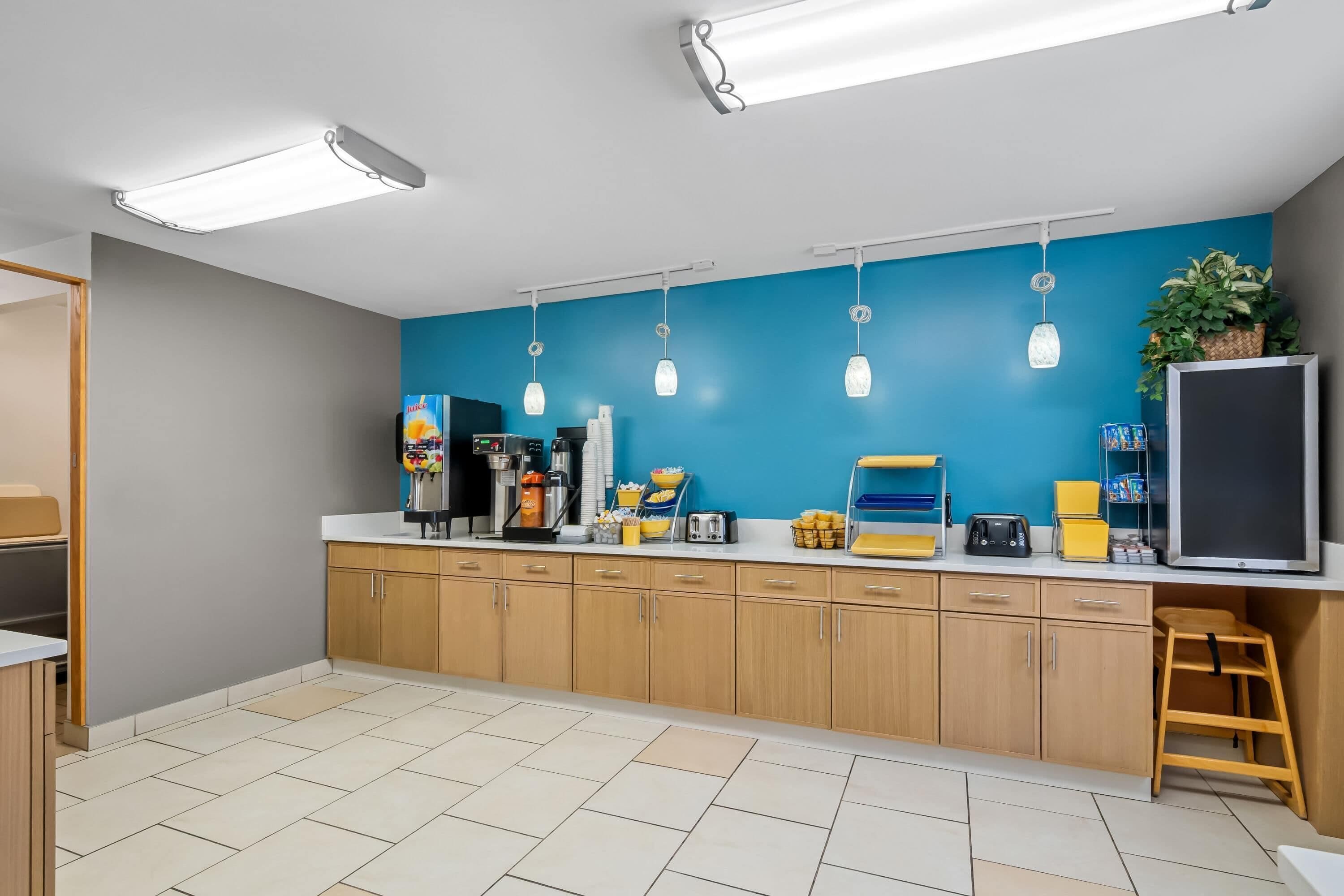 A modern kitchen with wooden cabinets, a blue accent wall, and various appliances.