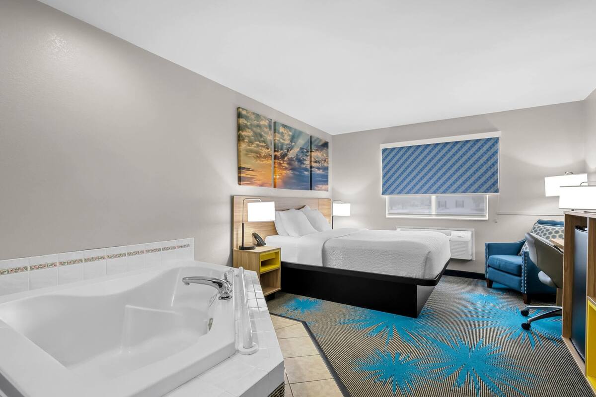 A hotel room with a large bed, a desk, a chair, a bathroom with a bathtub, and artwork on the walls.