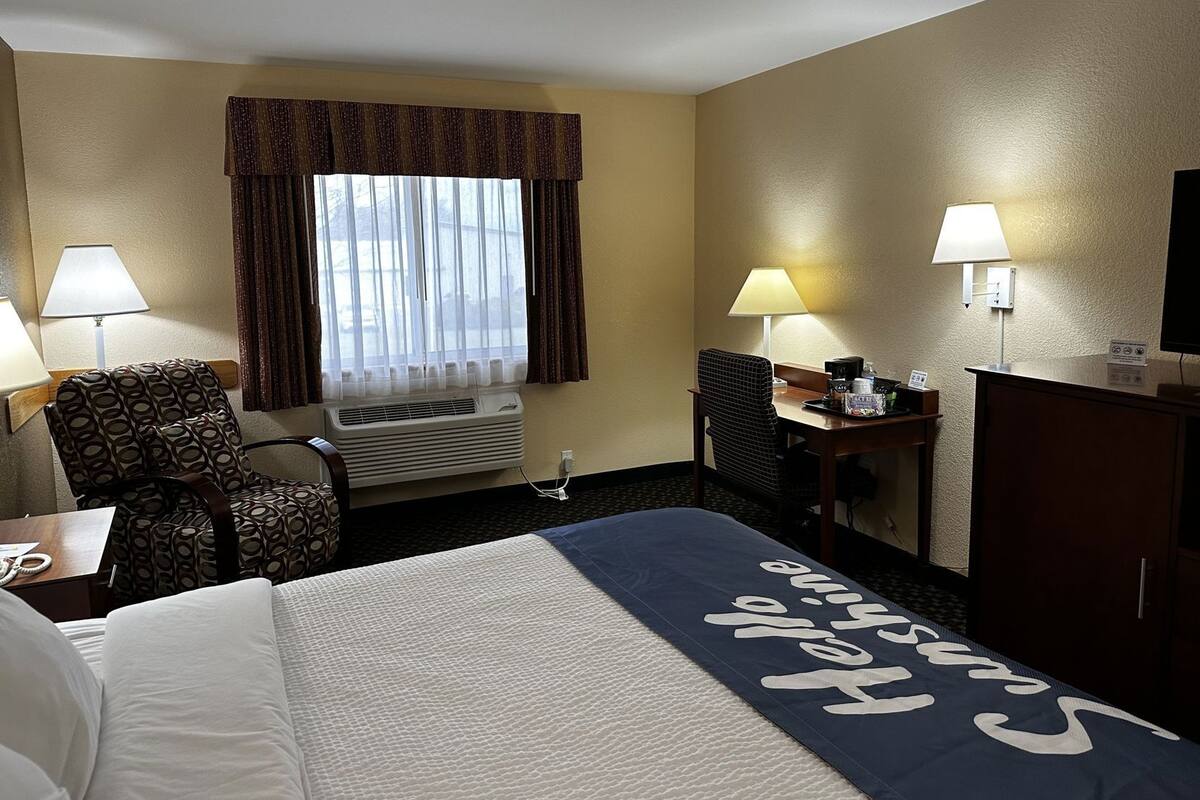 A hotel room with a bed, a desk, a chair, a TV, and a window with curtains.