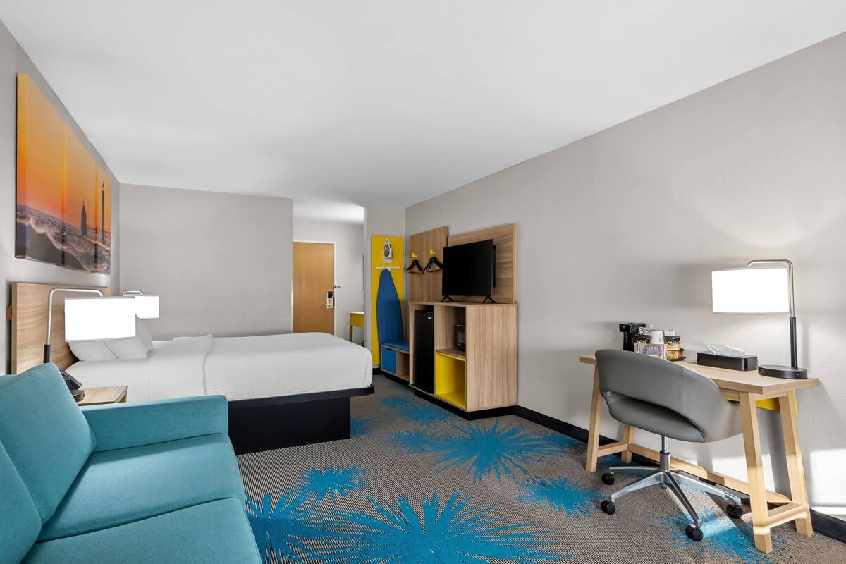 A hotel room with a bed, desk, chair, and a large painting on the wall.