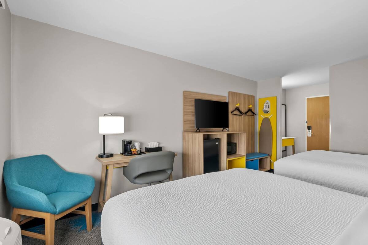 A hotel room with a bed, a desk with a computer, a chair, a TV, and a wardrobe.