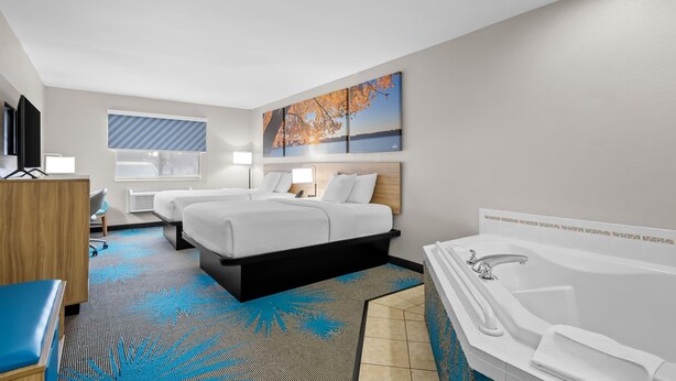A hotel room with two beds, a large window, a painting, a bathtub, and a desk. - Days Inn by Wyndham Imlay City (Imlay City)