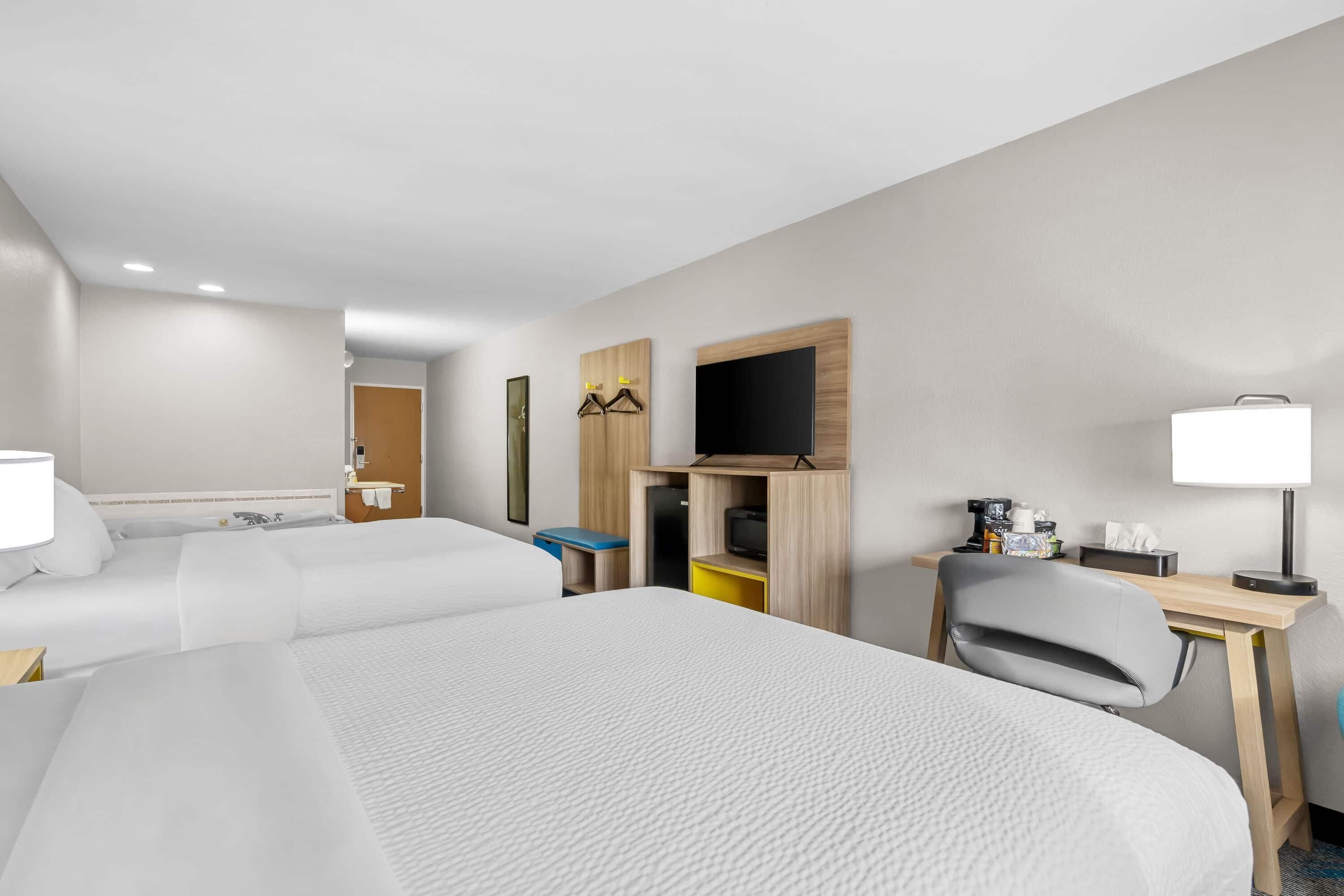 Habitación de hotel con dos camas, un escritorio con silla, un televisor y una pequeña mesa con lámpara.