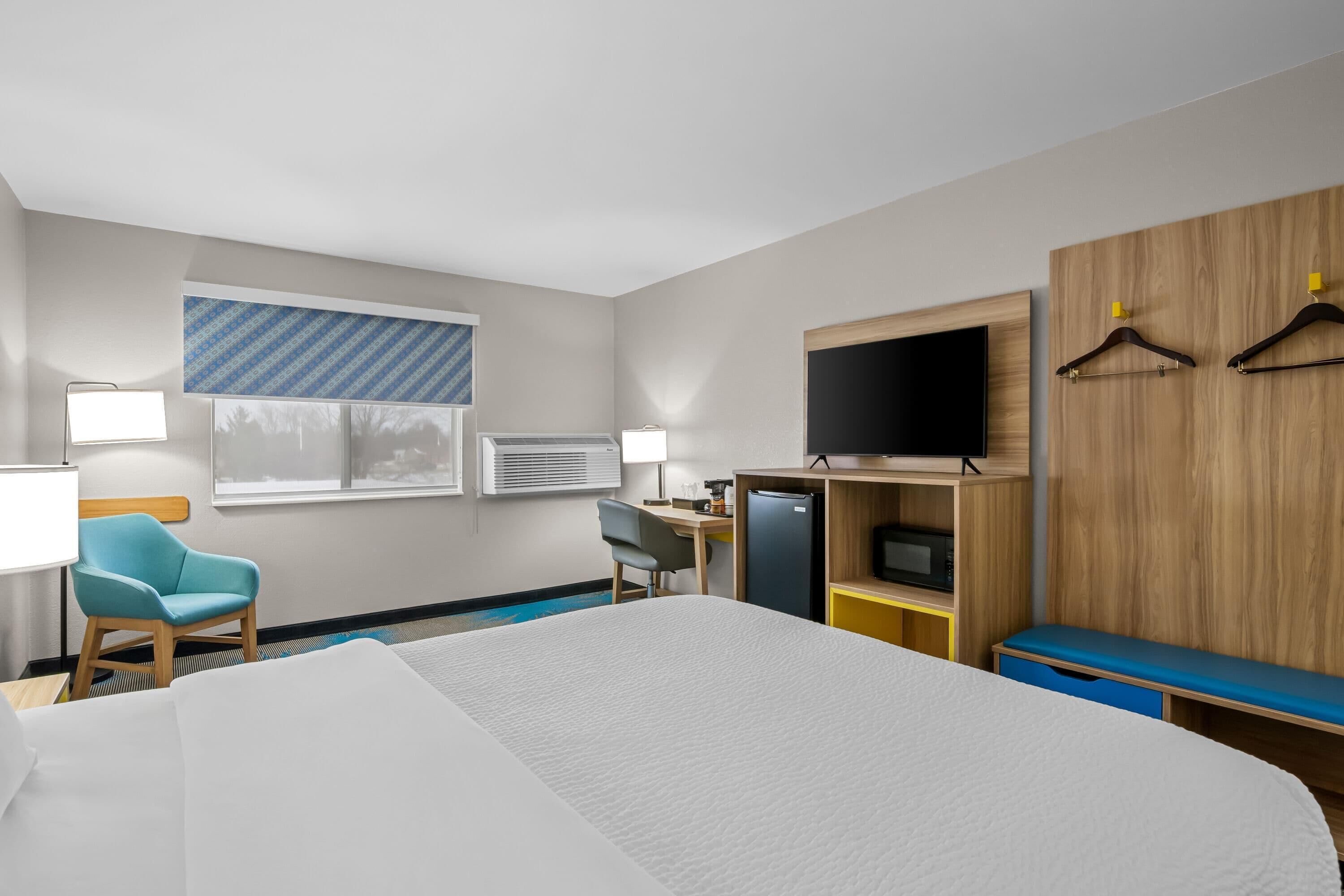 Une chambre d’hôtel moderne dotée d’un grand lit, d’un bureau avec un ordinateur, d’une télévision et d’un coin salon avec un banc.