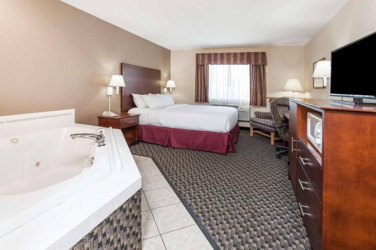 A hotel room with a large bed, a separate desk area, a television, and a bathroom with a bathtub.