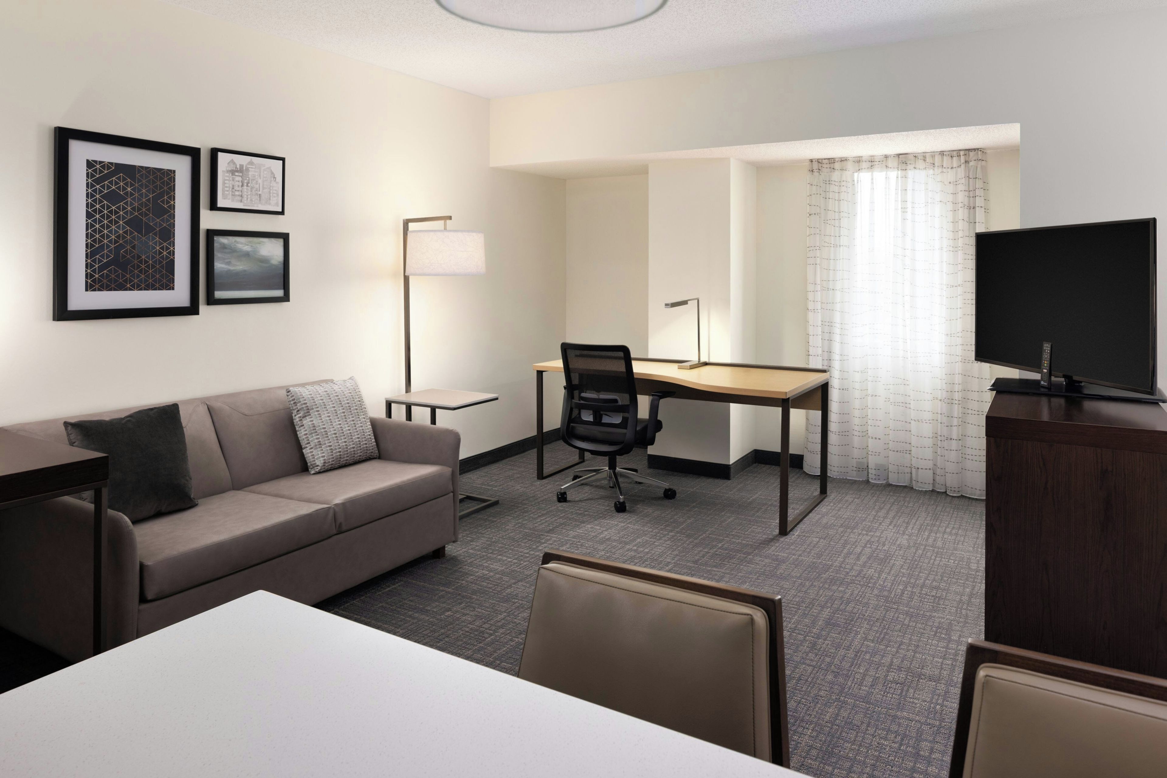 Habitación de hotel con sofá, escritorio, silla, televisión y cuadros en la pared.
