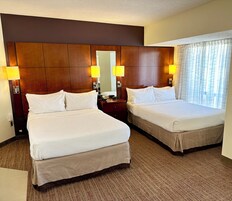 Habitación de hotel con dos camas, cabecera de madera, lámparas de noche y alfombra estampada.