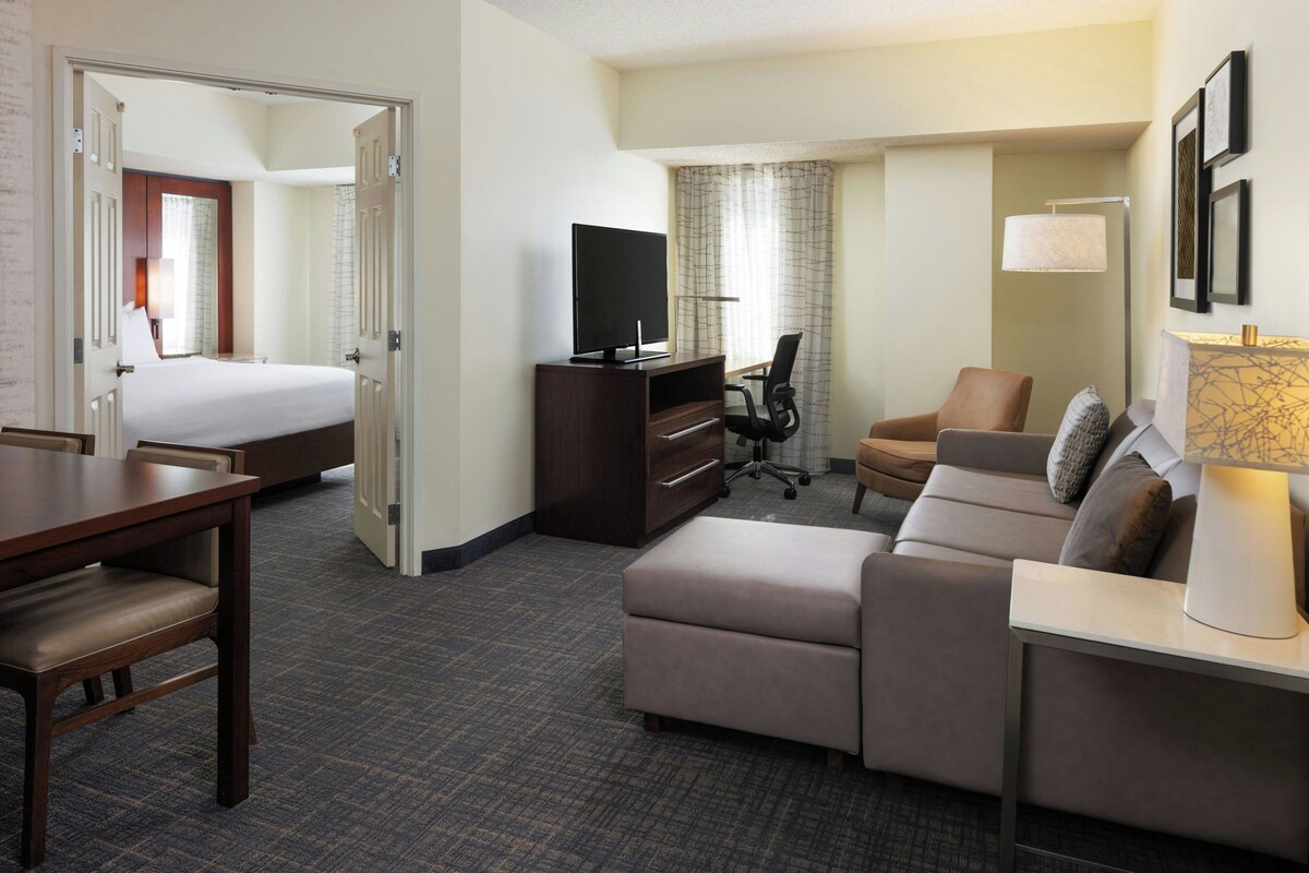 A hotel room with a bed, a desk, a sofa, a TV, and a lamp.