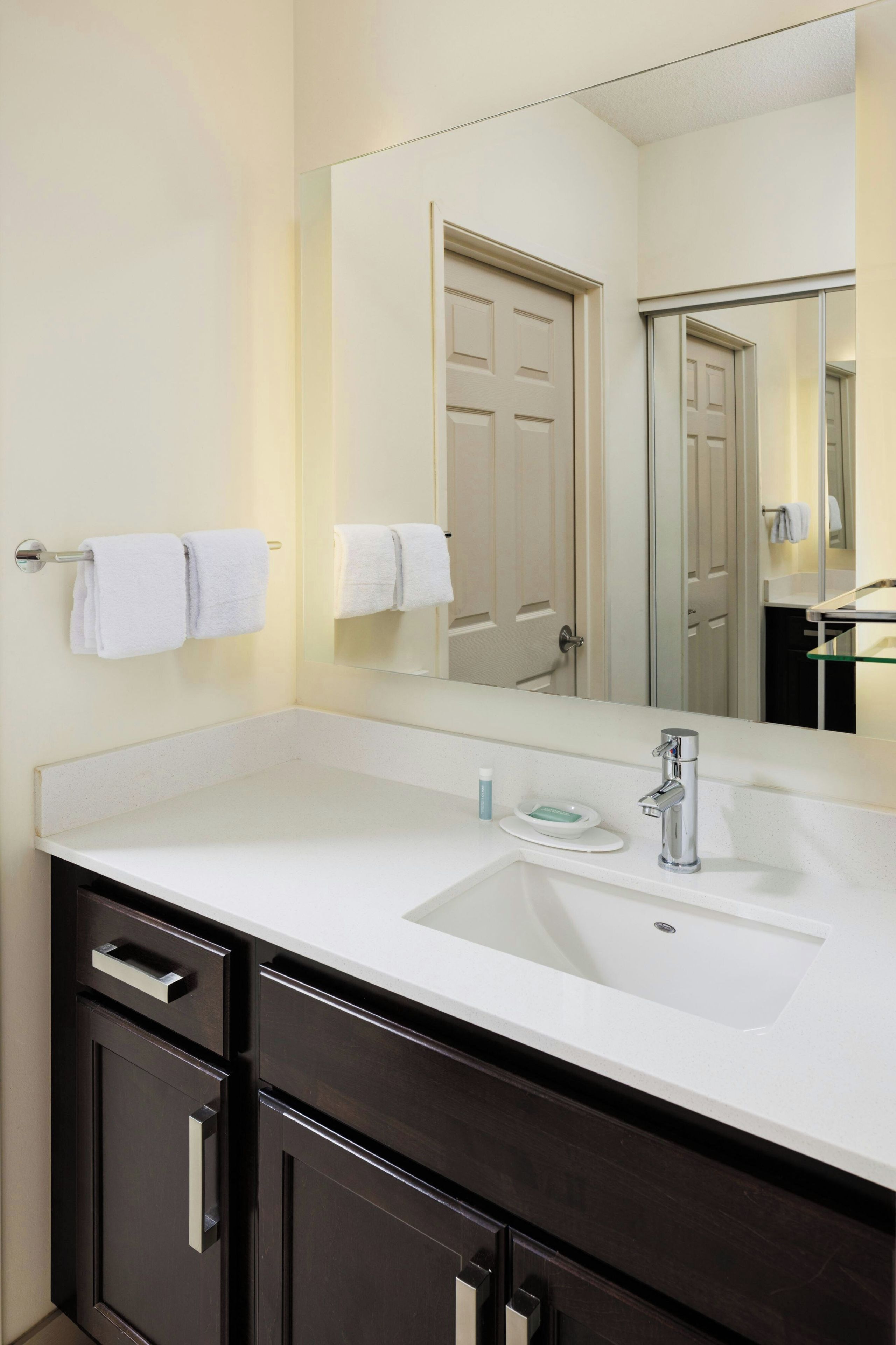 Un baño de hotel con un lavamanos blanco, tocador de madera oscura y un espejo grande.