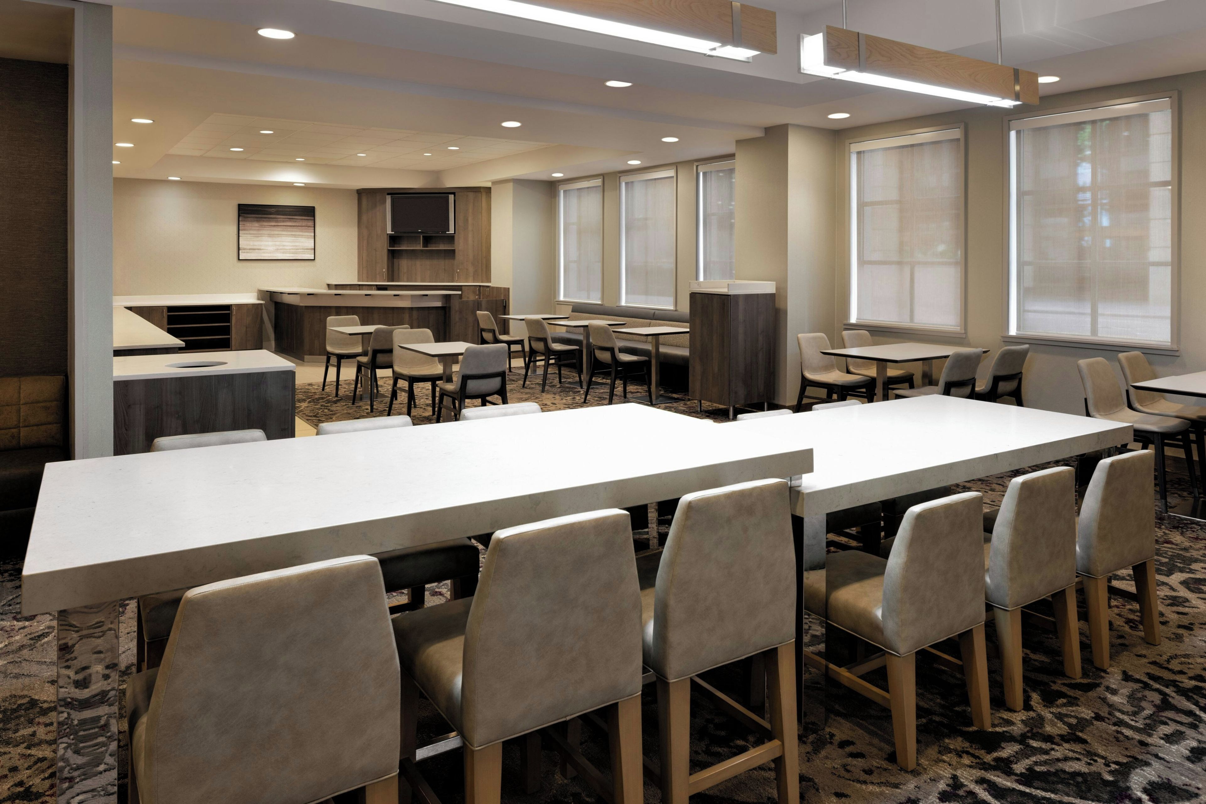 A hotel dining area with a long communal table, individual tables, and chairs.
