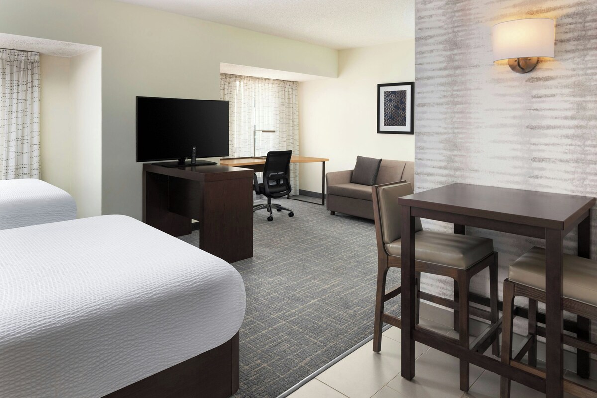 A hotel room with two beds, a desk with a computer, a television, a sofa, and a dining table.