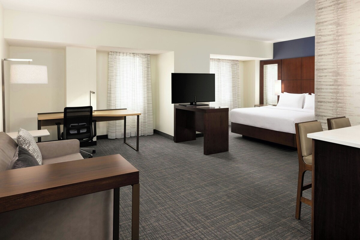 A hotel room with a bed, desk, chair, television, and a small table.