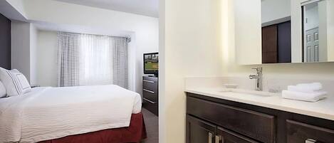 A hotel room with a bed, a bathroom with a sink and mirror, and a view of a field through the window.