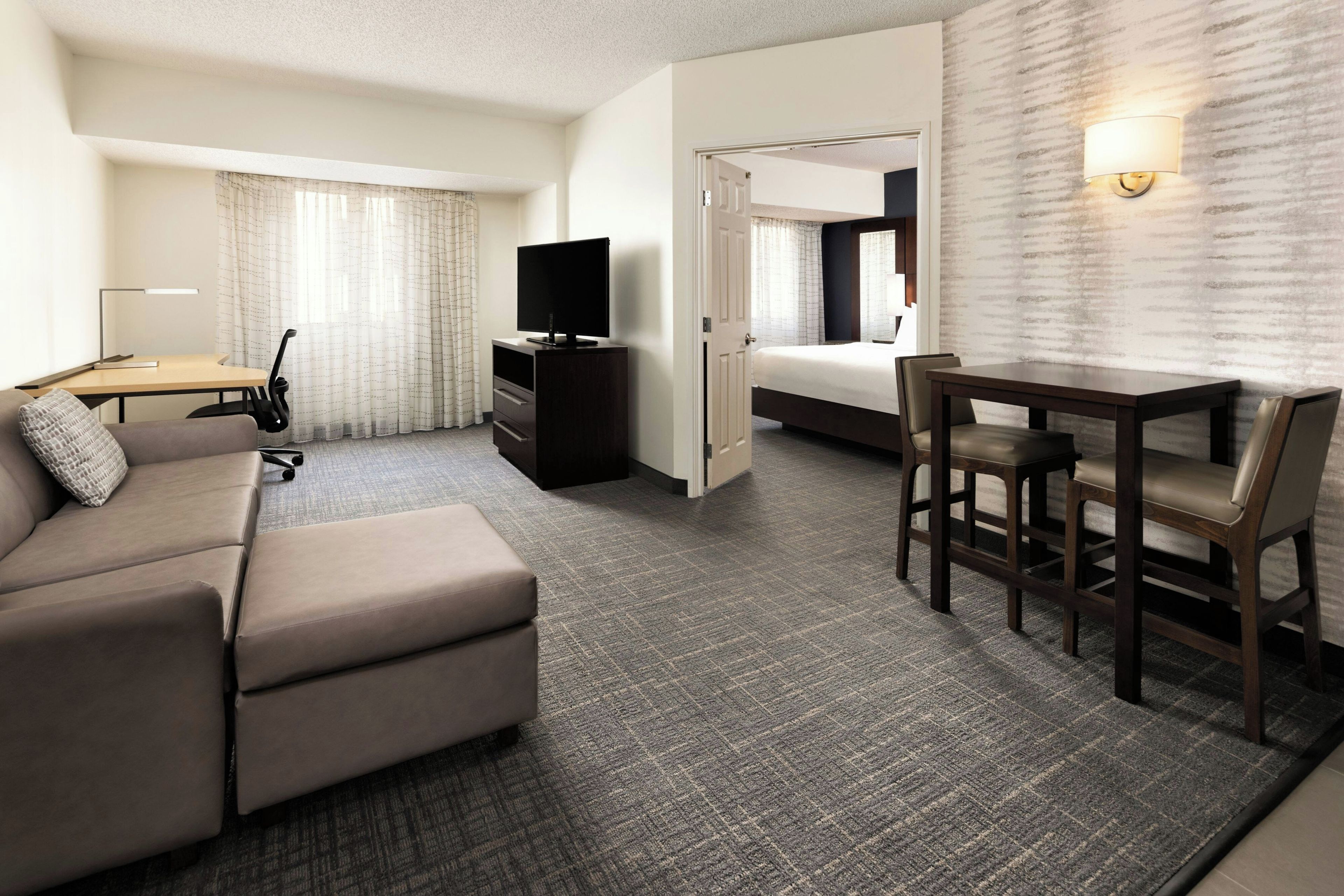 Habitación de hotel con sofá, escritorio con lámpara, televisión y cama.