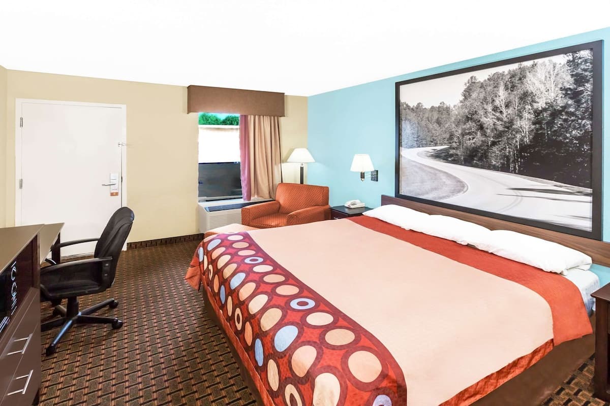 Une chambre d’hôtel avec un grand lit, un bureau avec une chaise, une fenêtre avec des rideaux et un tableau au mur.
