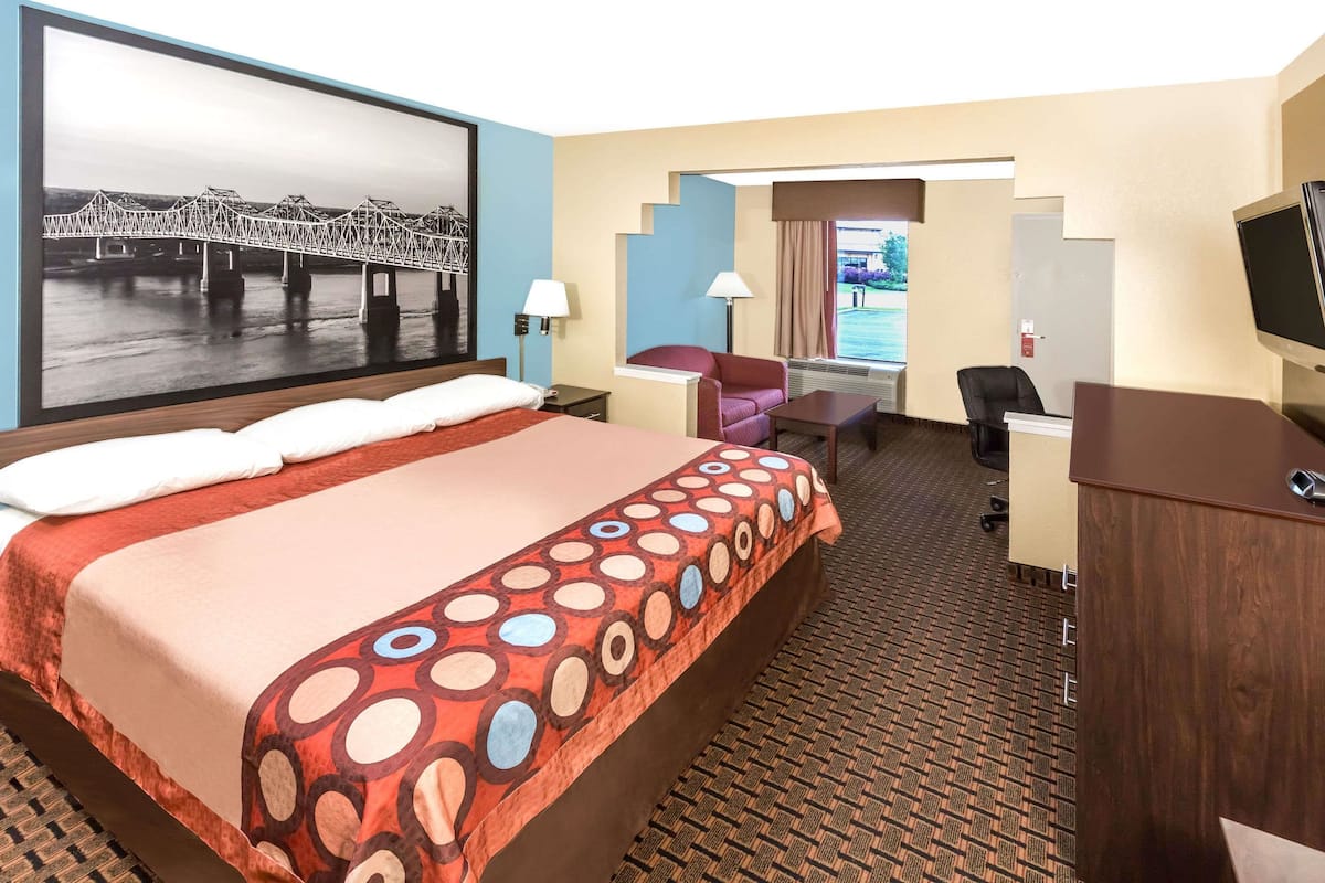 Une chambre d’hôtel avec un grand lit, un bureau, une chaise, une télévision et un tableau représentant un pont.