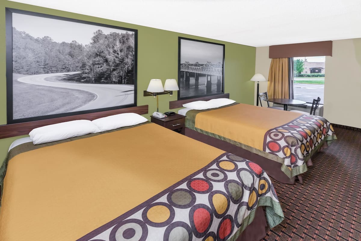 Une chambre d’hôtel avec deux lits, un bureau, une chaise, une lampe et une fenêtre donnant sur un pont et des arbres.