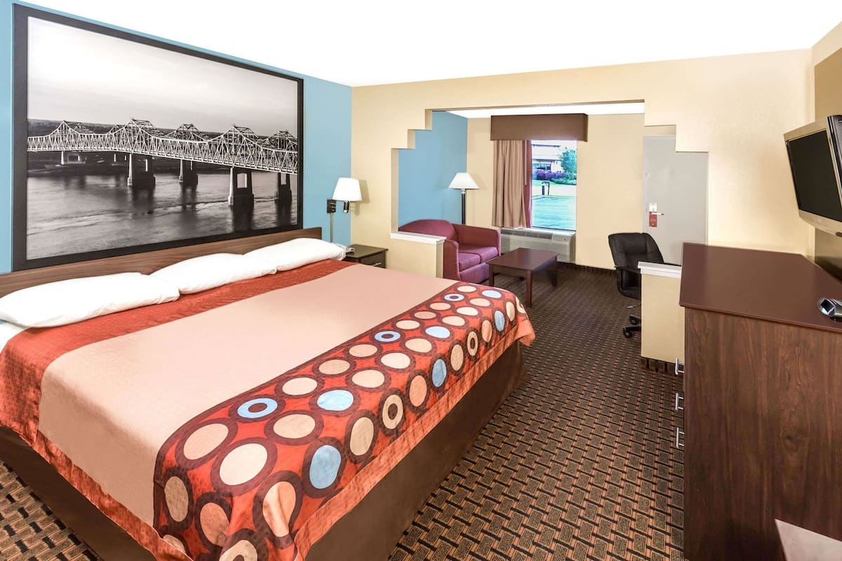 Une chambre d’hôtel avec un grand lit, un bureau, une chaise, une télévision et un tableau représentant un pont.