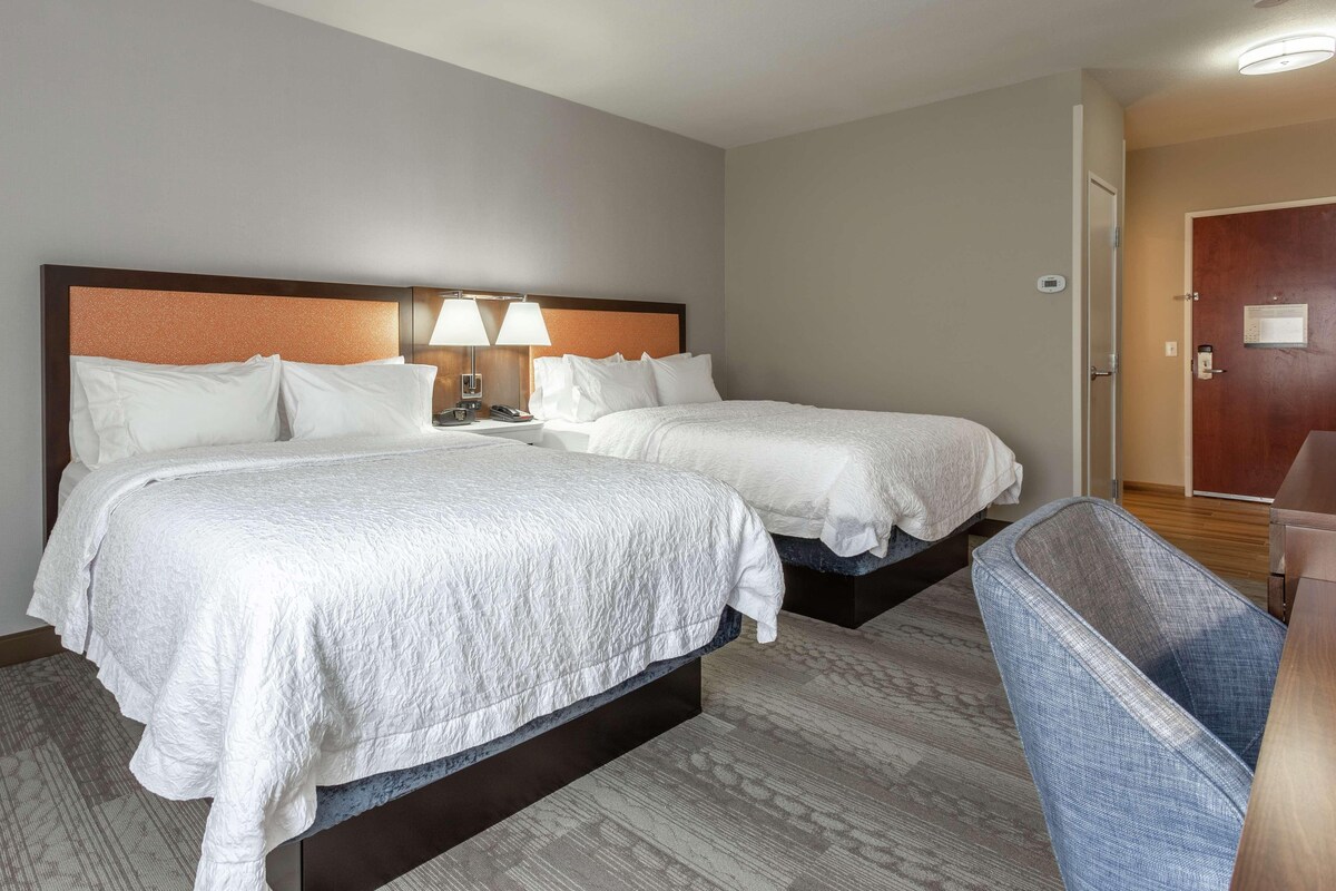 A hotel room with two beds, a desk, and a chair.