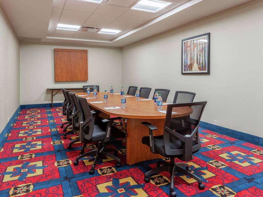 A conference room with a large wooden table, black chairs, water bottles, and a patterned carpet.