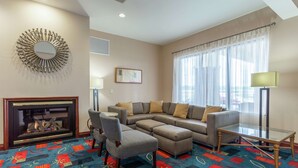 A living room with a sectional sofa, a fireplace, a patterned carpet, and a large window with sheer curtains. - Hampton Inn Jefferson City at Capital Mall (Jefferson City)