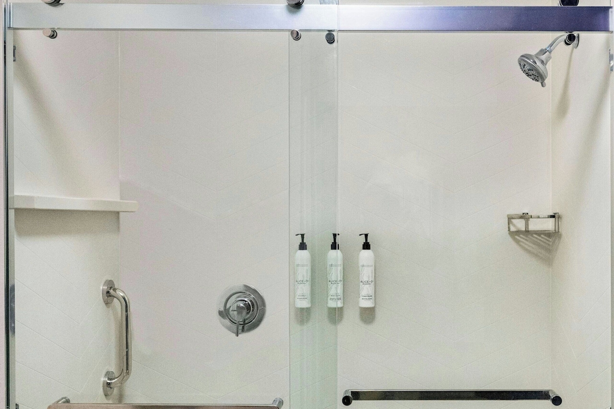 A glass-enclosed shower stall with a handrail, a shelf, and a towel rack.