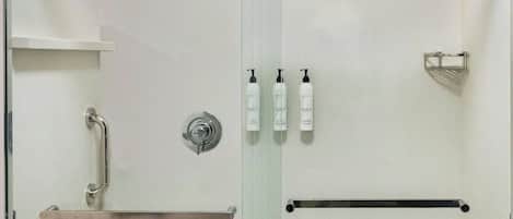 A glass-enclosed shower stall with a handrail, a shelf, and a towel rack.