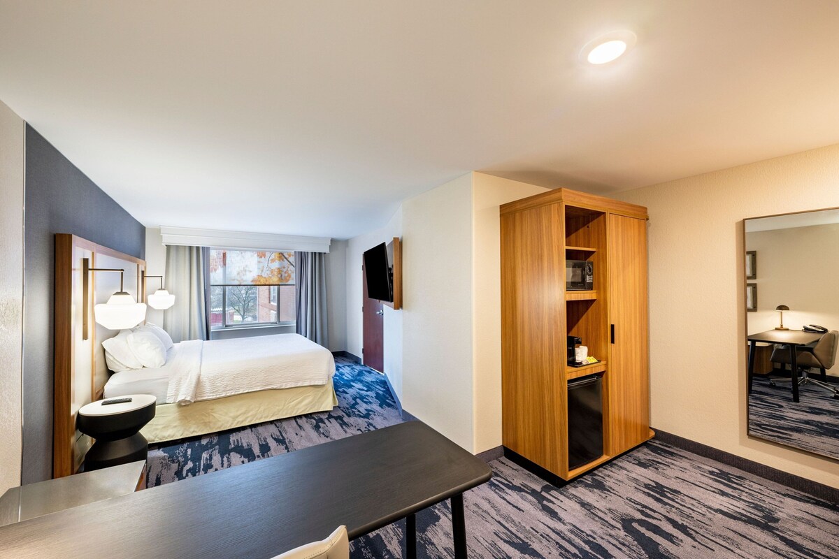 Une chambre d’hôtel comprenant un lit, une table de chevet, une lampe, une armoire et un bureau avec une chaise.
