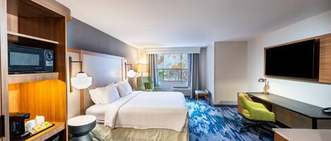 A hotel room with a bed, desk, TV, and a view of the outdoors.