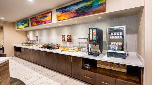 A hotel reception area with a counter, coffee machines, a refrigerated display, and artwork on the wall. - Fairfield Inn & Suites by Marriott St. Louis Chesterfield (Chesterfield)