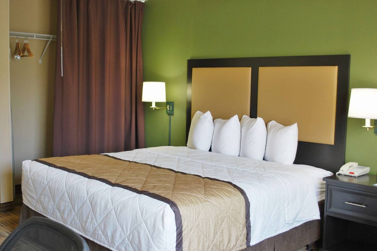 Hotellihuone, jossa on suuri sänky, kaksi yöpöytälamppua, puhelin ja naulakko.